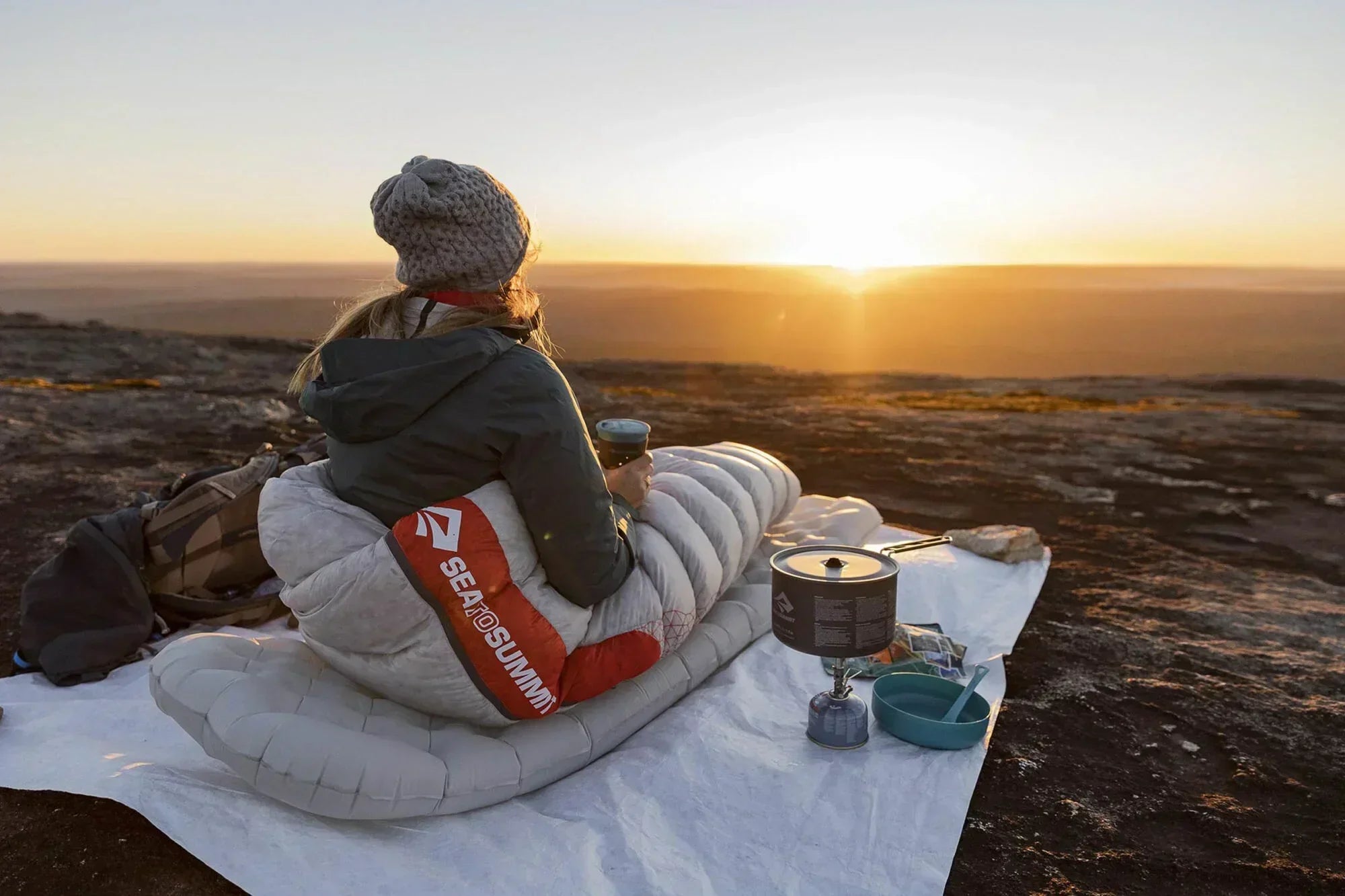 Sea To Summit outdoor campaign featuring a camper relaxing in a sleeping bag at sunset.
